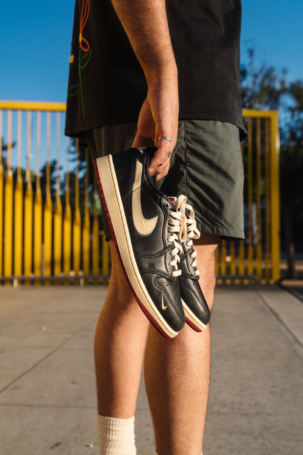 Black Nike SB Dunk Low sneakers held by person against yellow gate backdrop