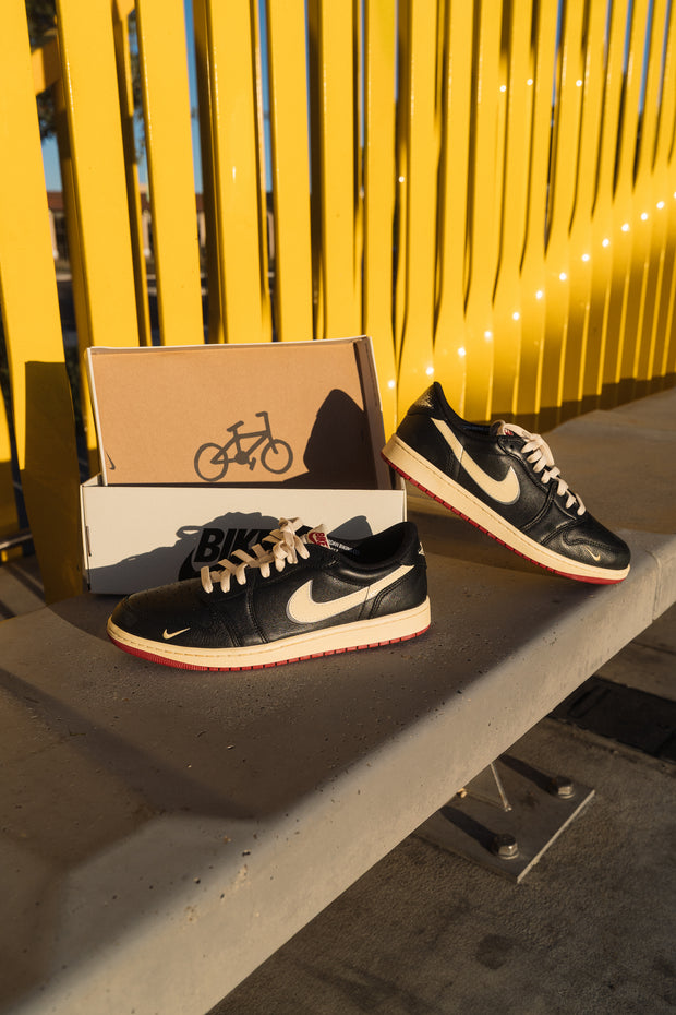 Black vintage Nike sneakers with cream swoosh and red soles on concrete bench