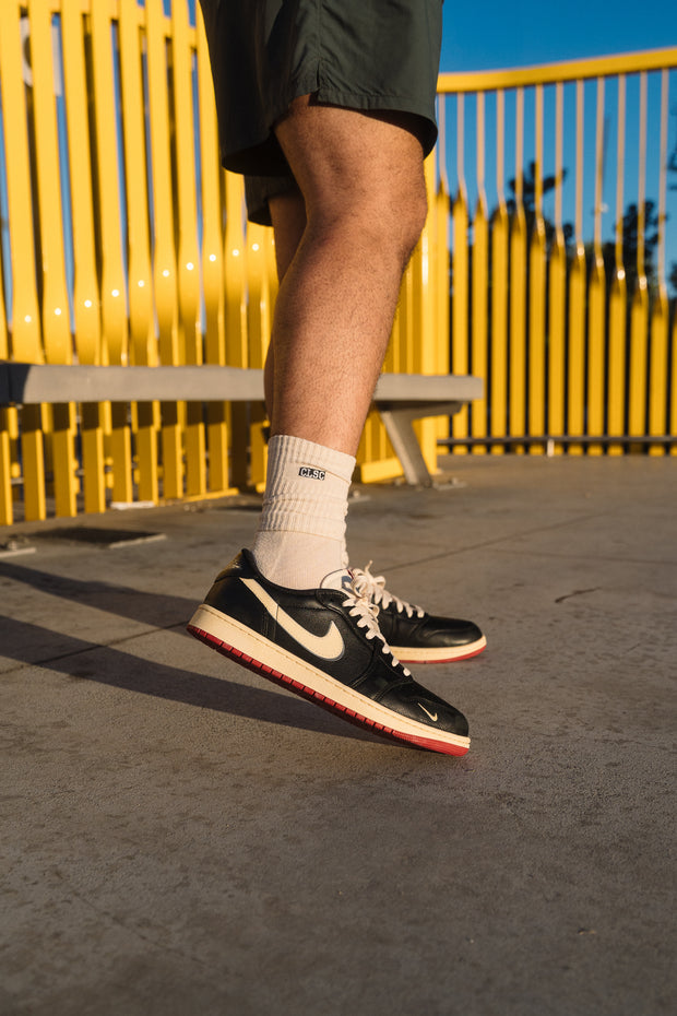 Black Nike SB Dunk Low sneakers on feet against yellow gate backdrop