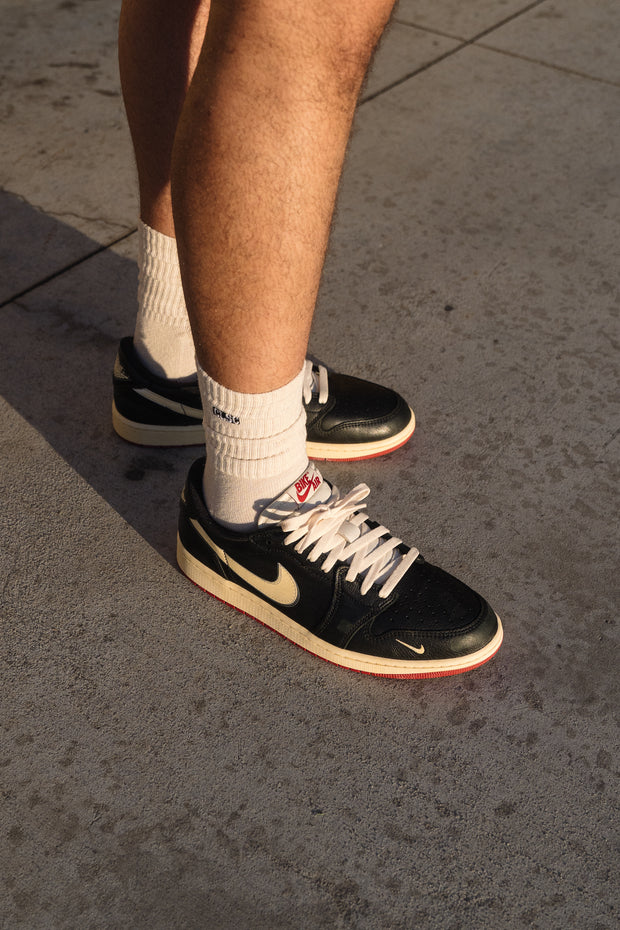 Black Nike SB Dunk Low sneakers on feet with cream swoosh and red outsole