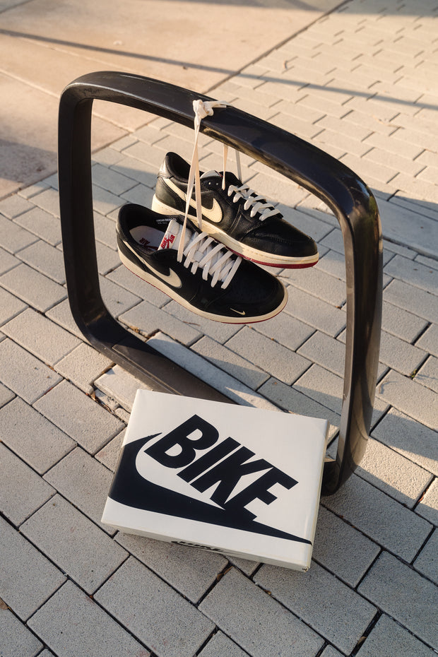 Black Nike SB Dunk Low sneakers hanging by laces over bike rack with shoebox