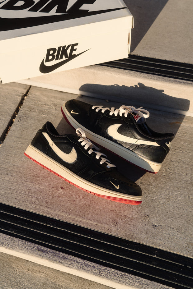 Black Nike SB Dunk Low sneakers with cream swoosh and red outsole near box