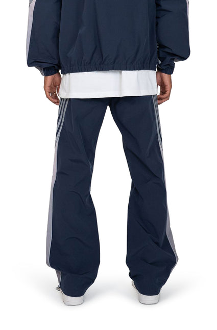 Rear view of navy EPTM Proxy pants featuring light gray side stripes and a relaxed fit in a smooth, matte finish fabric.