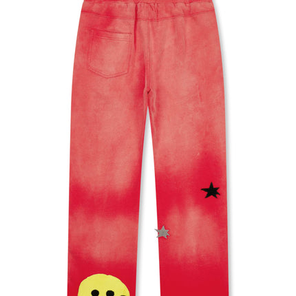 All Human 2+2=5 v2 sweatpants in red wash, featuring a yellow stitched smiley face and black and silver star patches.