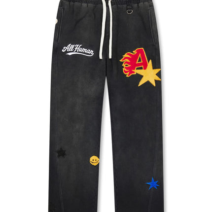 All Human Spitfire v2 sweatpants in black wash cotton featuring colorful embroidered flame, star, and smiley patches.