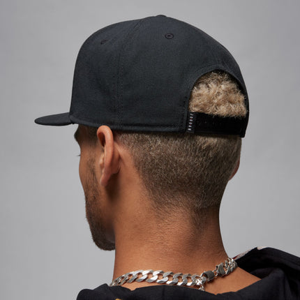Back view of a person wearing a black Jordan snapback cap, showing the textured fabric and adjustable closure strap.