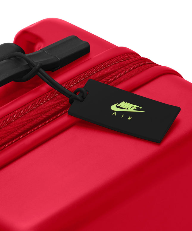 University red hardshell carry-on luggage with a black handle and a black Nike Air branded luggage tag attachment.