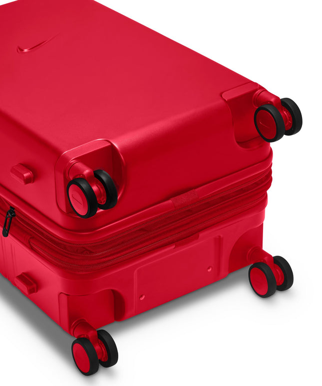 Bright university red hardshell Nike carry-on luggage viewed from an angle showing the black spinner wheels and zipper.