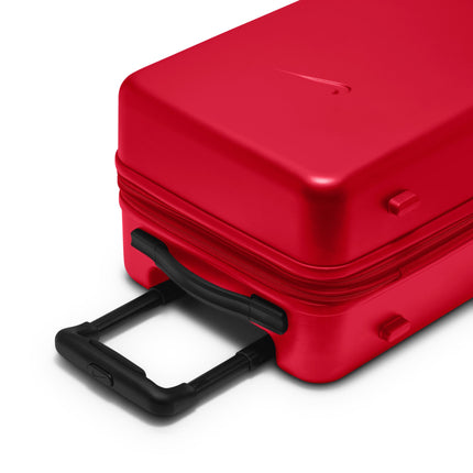 Bright red Nike carry-on luggage with a smooth, hard-shell finish and a black extendable handle, viewed from an angle.