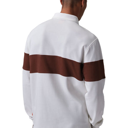 Back view of a man wearing a Nike Jordan Brooklyn rugby shirt in white and bronze with brown pants on white background.