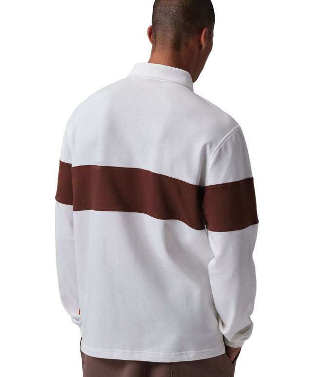 Back view of a man wearing a Nike Jordan Brooklyn rugby shirt in white and bronze with brown pants on white background.