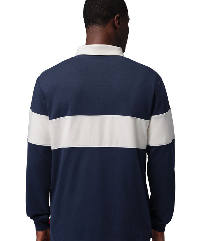Back view of a man wearing a navy blue Nike Jordan long-sleeve cotton rugby shirt featuring a wide white chest stripe.
