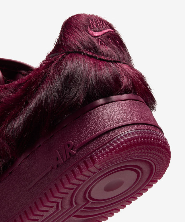 Close-up of a burgundy Team Red Nike Air Force 1 sneaker featuring a shaggy faux fur upper and textured rubber sole.