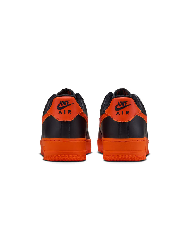 Back view of Nike Air Force 1 '07 men's sneakers in black leather with vibrant orange heel tabs and rubber soles.