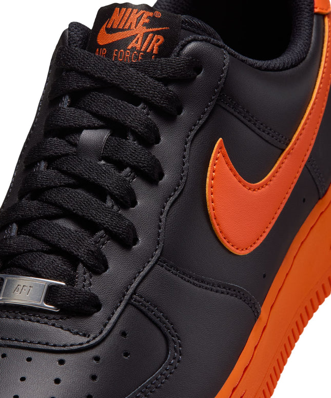 Close-up of a black leather Nike Air Force 1 07 shoe with a vibrant orange Nike swoosh and matching orange midsole.