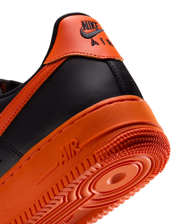 Close-up of the black leather heel and vibrant orange midsole of a Nike Air Force 1 '07 sneaker on a white background.
