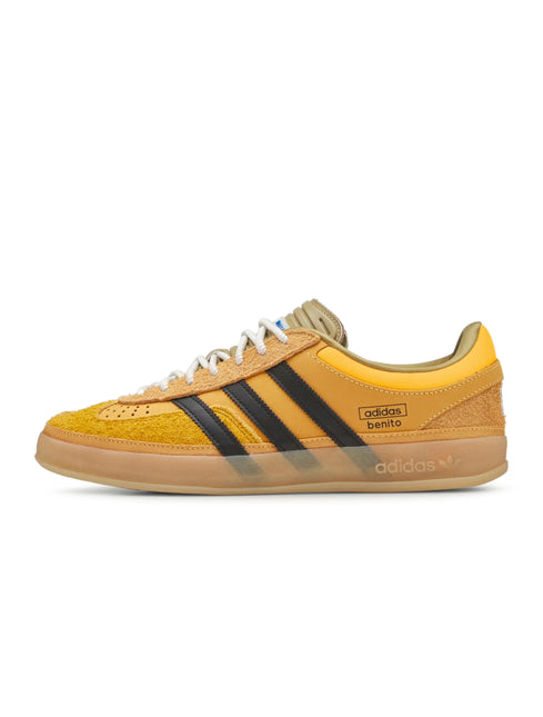 Side view of a gold suede Adidas Gazelle Indoor sneaker with black three stripes, white laces and a gum sole.