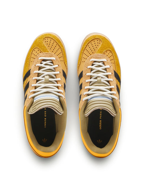 Top-down view of a pair of gold suede Adidas Gazelle Indoor sneakers with black three stripes and white laces.
