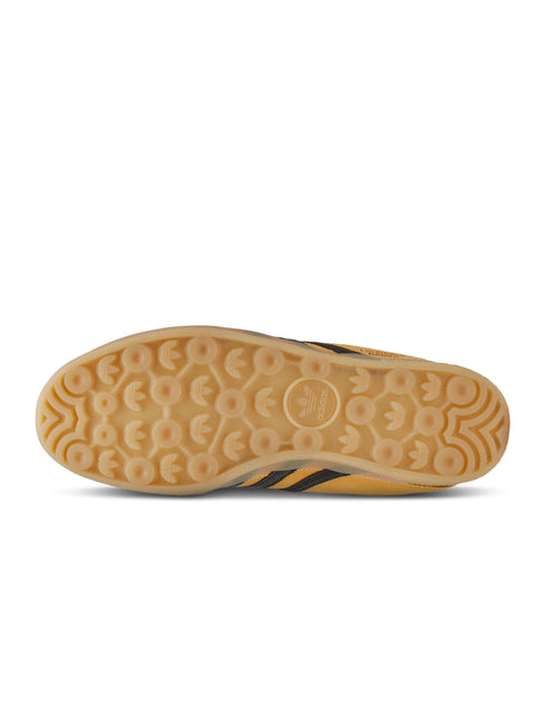Bottom view of a gold Adidas Gazelle Indoor sneaker showing the tan gum rubber outsole with circular tread pattern.