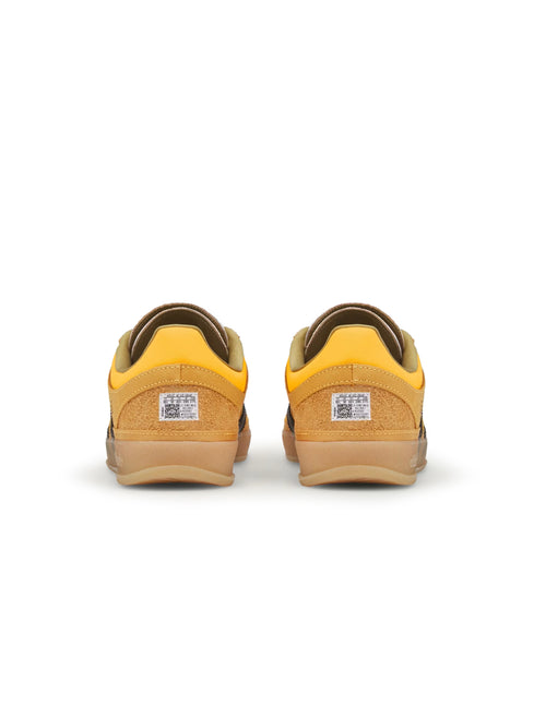 Rear view of a pair of gold suede Adidas Gazelle Indoor sneakers showing the heel tabs and gum soles.