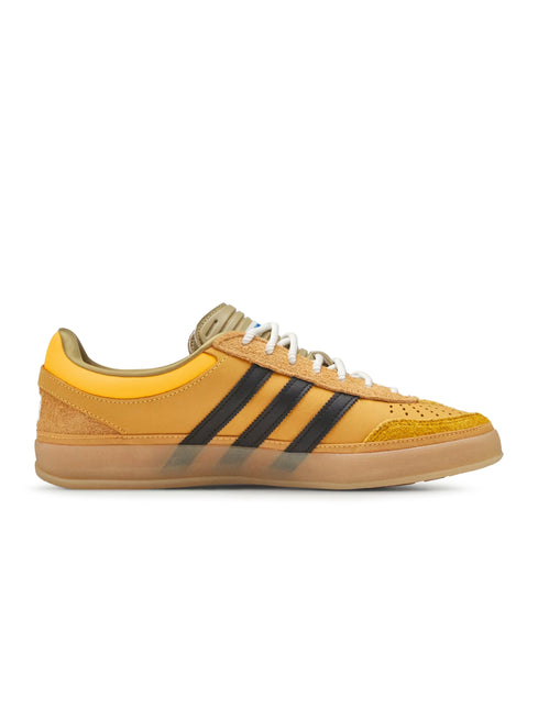 Side view of a single gold suede Adidas Gazelle Indoor sneaker with black three stripes, white laces and a gum sole.