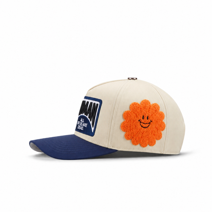 All Human THE CURE cap in cream cotton with a navy blue brim, featuring a large orange fuzzy flower smiley patch.