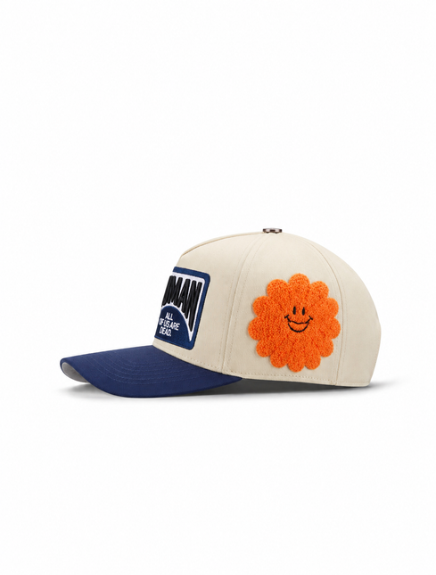 All Human THE CURE cap in cream cotton with a navy blue brim, featuring a large orange fuzzy flower smiley patch.