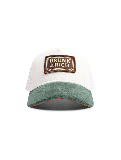Front view of a white baseball cap with a green corduroy brim and a brown Drunk & Rich patch.