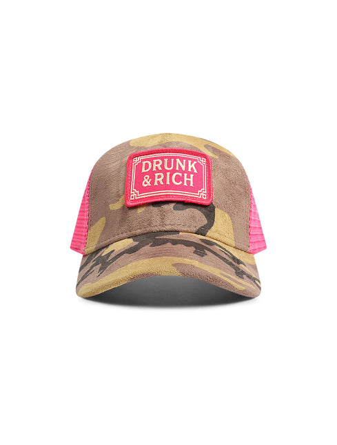 A camouflage trucker hat with a bright pink mesh back and a pink patch on the front that reads 'DRUNK & RICH'.