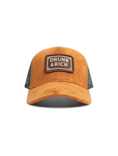 Brown suede trucker hat featuring a rectangular Drunk & Rich patch on the front with dark green mesh side panels.