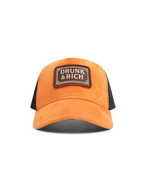 Orange suede trucker hat with black mesh back panels and a brown rectangular patch featuring the Drunk & Rich logo.