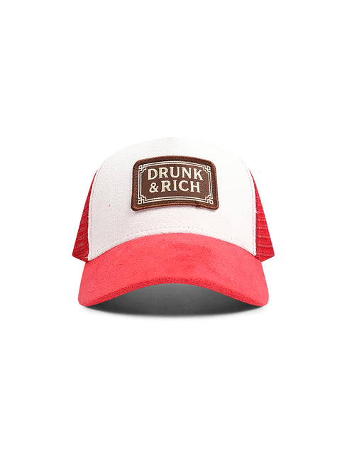 A red and white trucker hat with a brown leather patch on the front that reads 'DRUNK & RICH'.