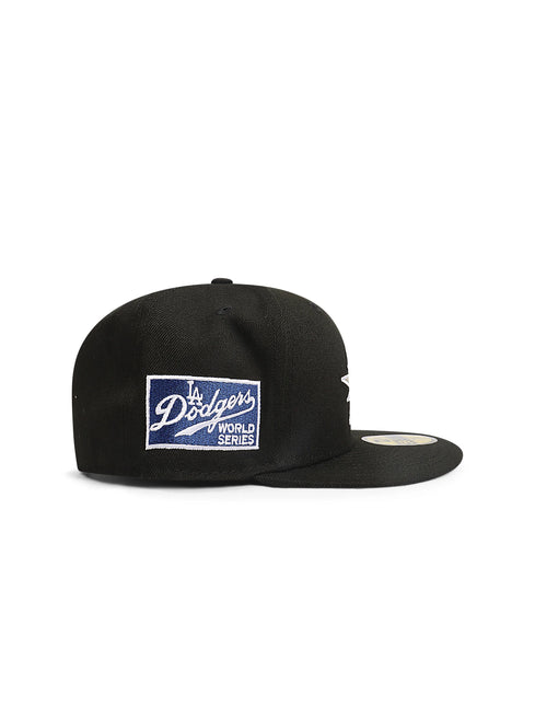 Side view of a black fitted baseball cap with a blue and white Dodgers patch on the side panel.