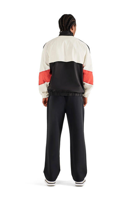 Back view of a person wearing a Malbon Axis cream and black zip-up track jacket with red sleeve stripes and black pants.