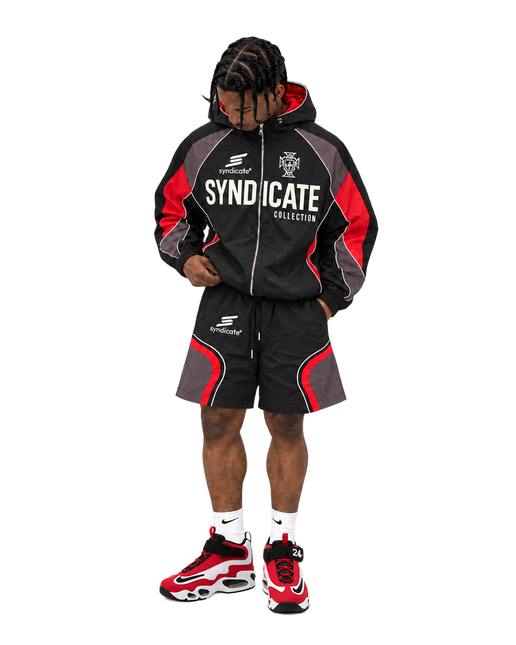 Model wearing a black Syndicate nylon tracksuit with red and gray accents and matching shorts against a white background.